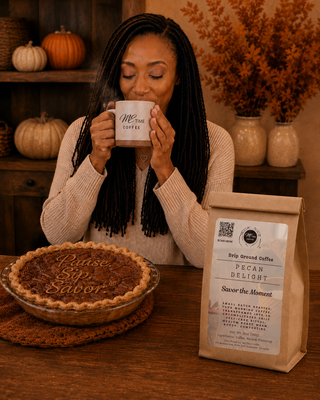 A woman with long black braids sits at a wooden table, holding a white mug that reads 'Me Time Coffee.' In front of her is a bag of Pecan Delight drip coffee and a pie on a crocheted mat.