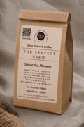 A brown kraft paper coffee bag standing upright on a soft gray fabric surface. The front label reads 'The Perfect Brew' and shows the Me Time Coffee brand logo and QR code.